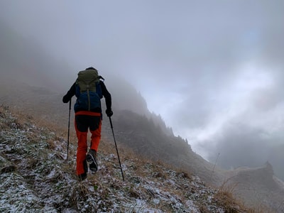 Wearing green jacket and red backpack man walking along the rock
